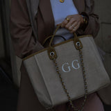 Woman holding a beige Canvas Tote Bag with Chain Beach bag featuring the letter GG on it.