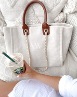 A woman is sitting on a couch holding a coffee and a tote bag.
